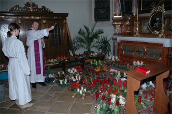 ein Pfarrer segnet am Boden stehende Adventkränze